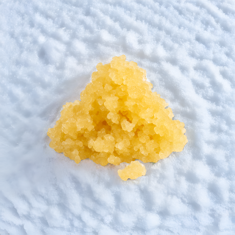 Gelbes Sugar Wax CBD Dab, 1g, auf weißem Hintergrund, präsentiert die körnige Textur und leuchtende Farbe des Produkts.