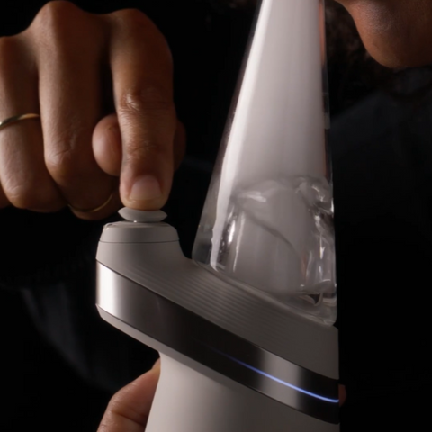 Person aktiviert den Puffco Peak Smart E-Rig Dab Vaporizer, während Rauch im Glasaufsatz sichtbar ist.