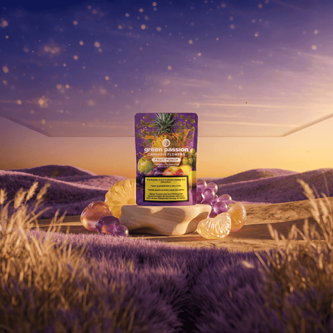 Green Passion Cannabis Flowers Fruit Punch – violette 10g Indoor-Packung auf Holzsockel in lavendelfarbenem Feld bei Sonnenuntergang, umgeben von gläsernen Früchten (Ananas, Trauben, Mandarine).