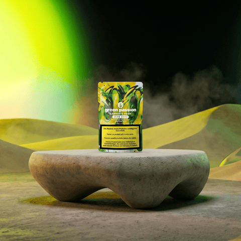 Green Passion Cannabis Hash Zero Zero – gelb-grüne Packung auf geschwungenem Betonsockel in gelbgrüner Nebellandschaft mit abstraktem Oliven-Motiv auf der Verpackung.