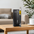 CBD Vape-Set "Cookies" on a wooden table, consisting of a black vape pen and packaging, in a modern living room with a sofa and plants in the background.