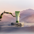 DOLOCAN CBD Hand Cream in einer grünen Tube auf einem Stein vor einer Berglandschaft.