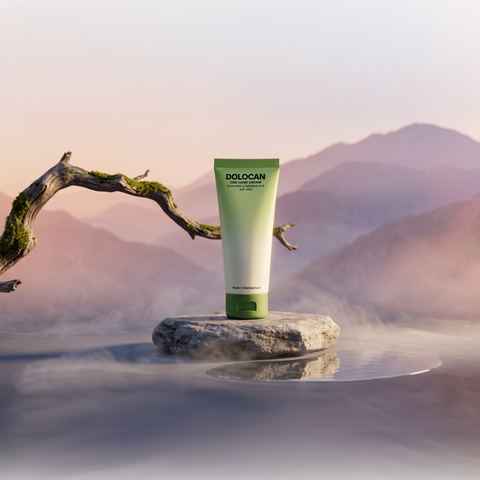 DOLOCAN CBD Hand Cream in einer grünen Tube auf einem Stein vor einer Berglandschaft.