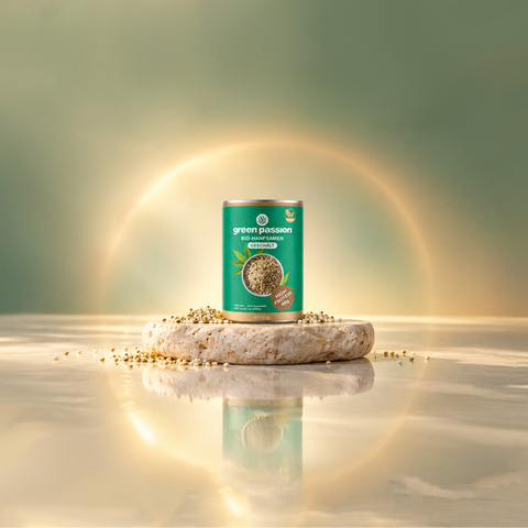 Dose mit Bio-Hanfsamen von Green Passion auf einem Steinpodest, umgeben von einigen losen Samen, vor einem weichen, grünlichen Hintergrund.
