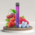 Lila Elfbar 600v2 vape con decorazioni di fragola, lampone, ciliegia e cubetti di ghiaccio su piedistallo di legno, piacere fruttato in primo piano.